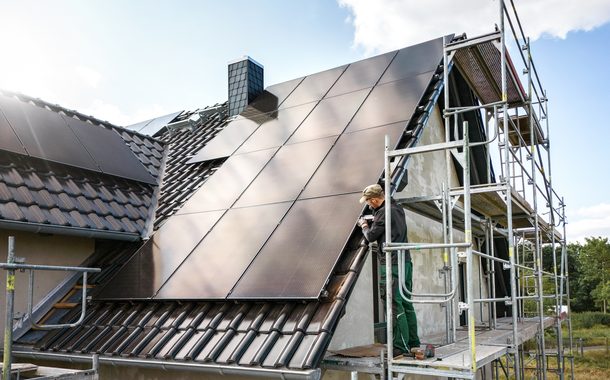 Techniker steht auf einem Gerüst, während er an einem Solarpanel eines Einfamilienhauses in Deutschland arbeitet.